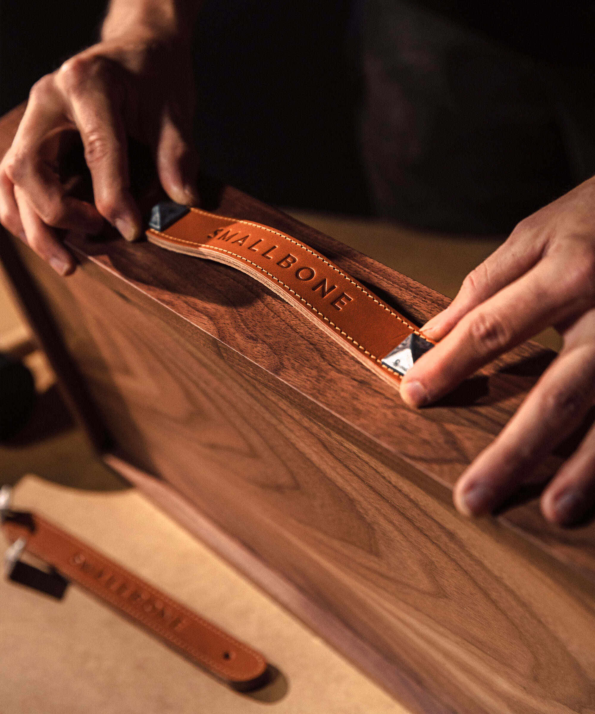 a craftsman applying a Smallbone tan leather pull handle to an American walnut draw front